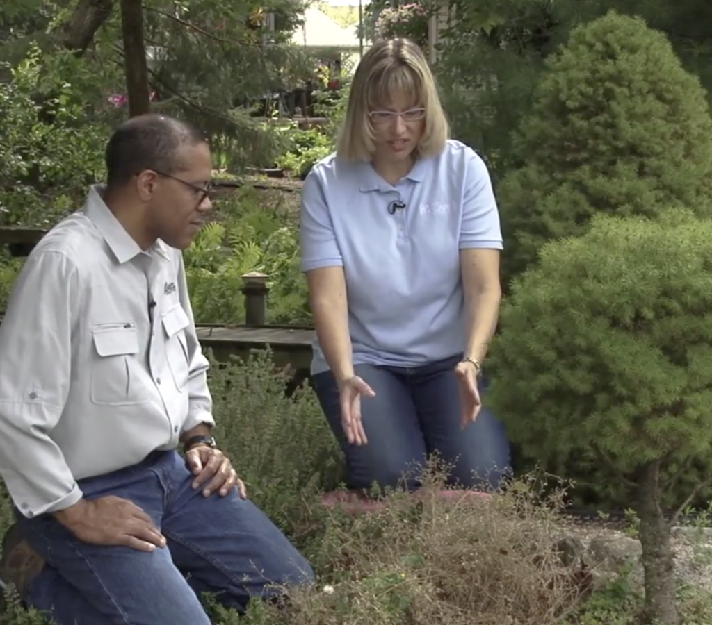 Man and women kneeling to inspect plants on a garden railroad.