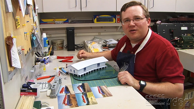 Cody Grivno sitting at his workbench with a scratchbuilt freight house