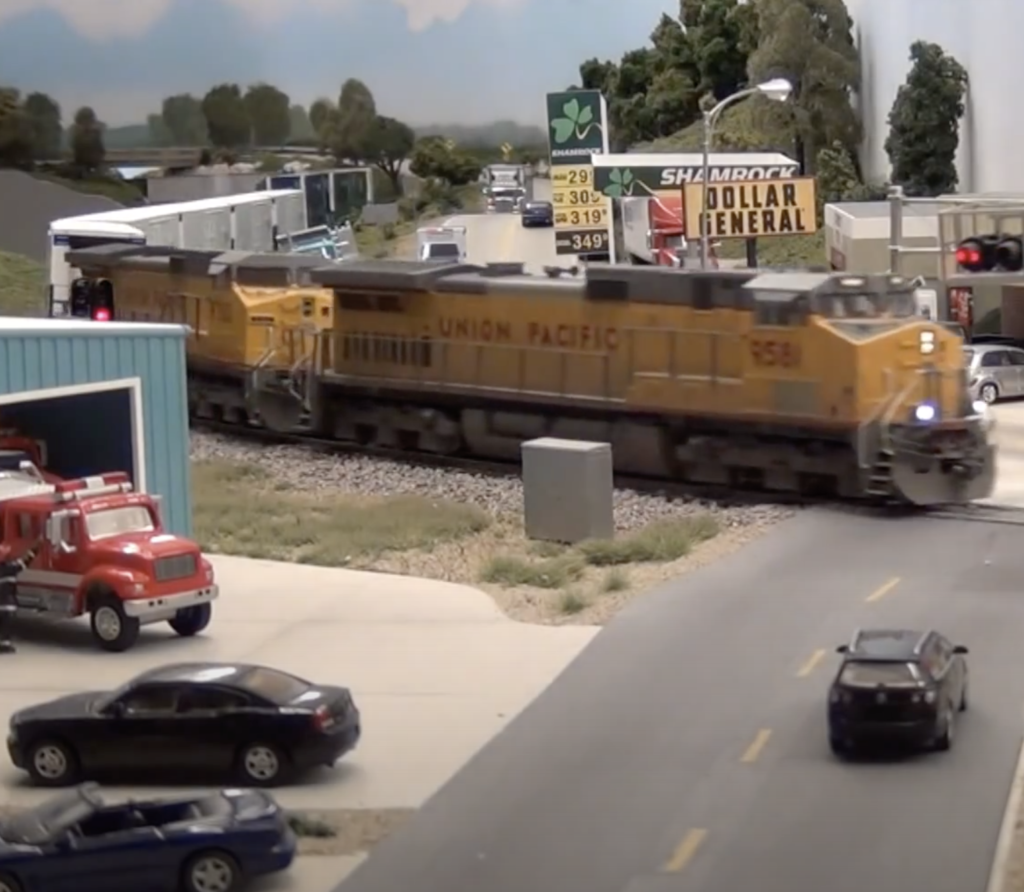Yellow model Union Pacific locomotives lead a freight train through a low-density urban commercial corridor.