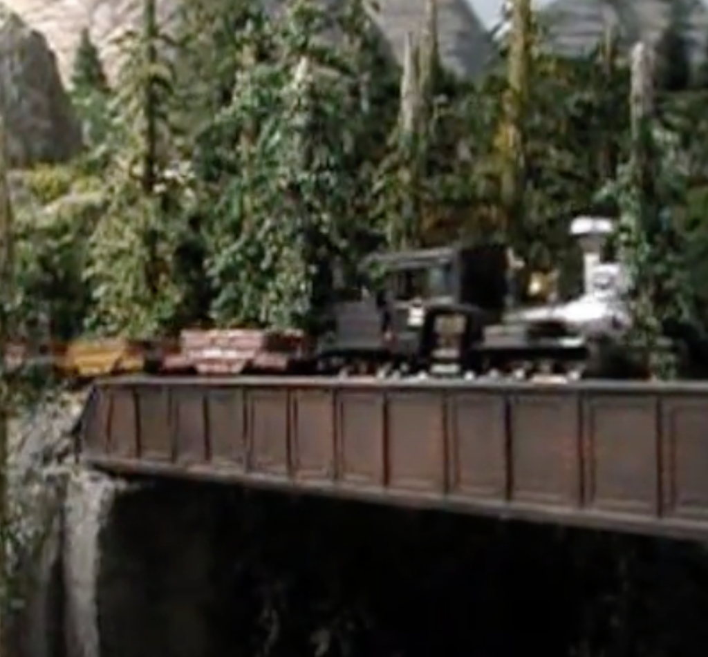 A model logging steam locomotive and train working over a bridge.