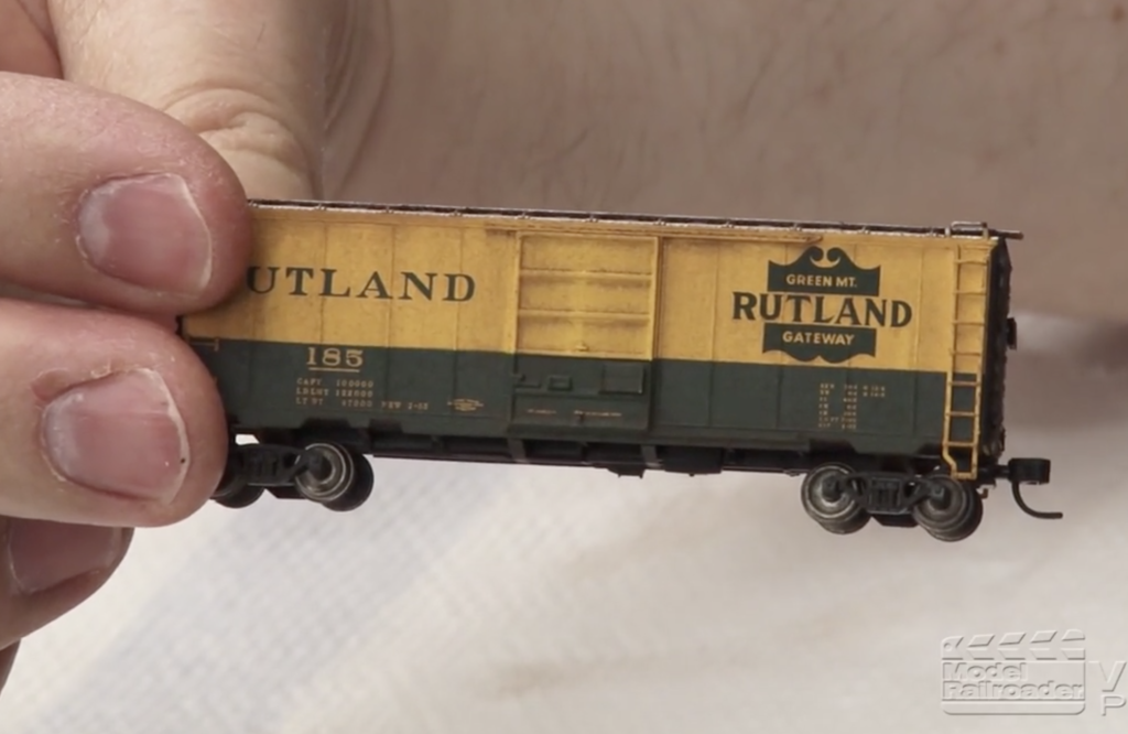 Fingers hold a small scale model boxcar.