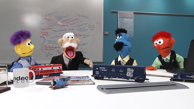 Four puppets sitting around a table with model trains