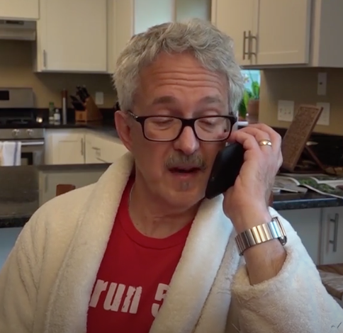 Man wearing glasses and bathrobe talking on a phone.