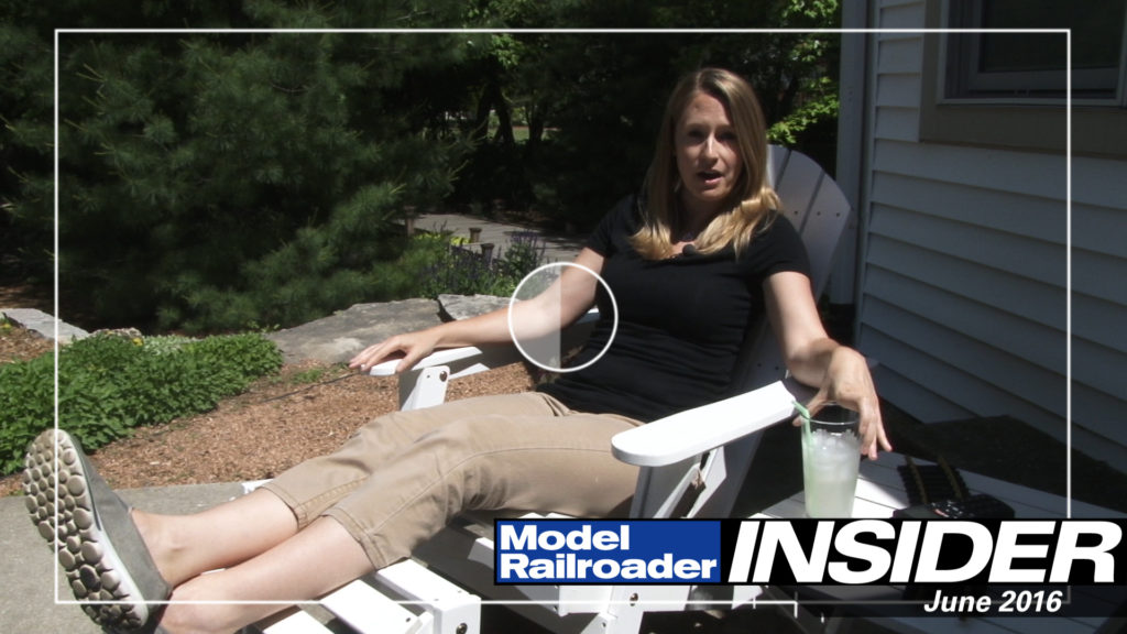 Jenny Freeland relaxing in a chair with a glass of lemonade next to Kent Johnson's garden railroad