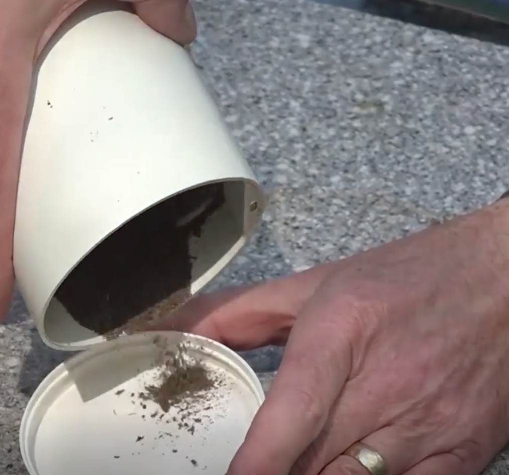 Two hands working to pour a powdery brown substance into a plastic lid.