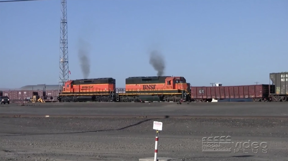 Two orange-painted switching locomotives work in a yard under cloudless skies.