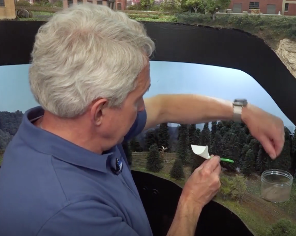 Man with back turned to camera works on lower level of a multi-level model train layout.