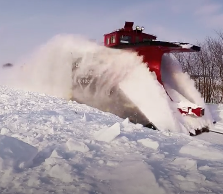 Red railroad snowplow spraying snow to each side of the tracks.