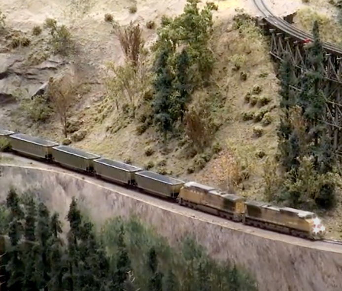 Yellow Union Pacific-style model locomotives lead a coal train on a Western US-themed layout.