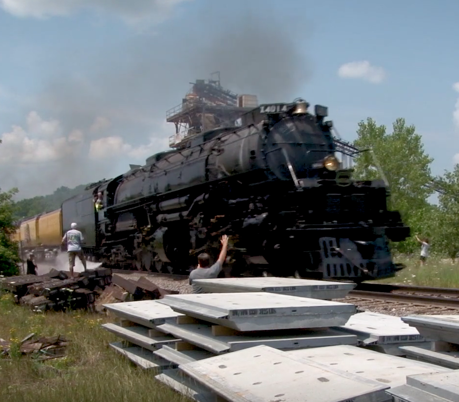 4-8-8-4 steam locomotive moves at speed while rail fans look on.