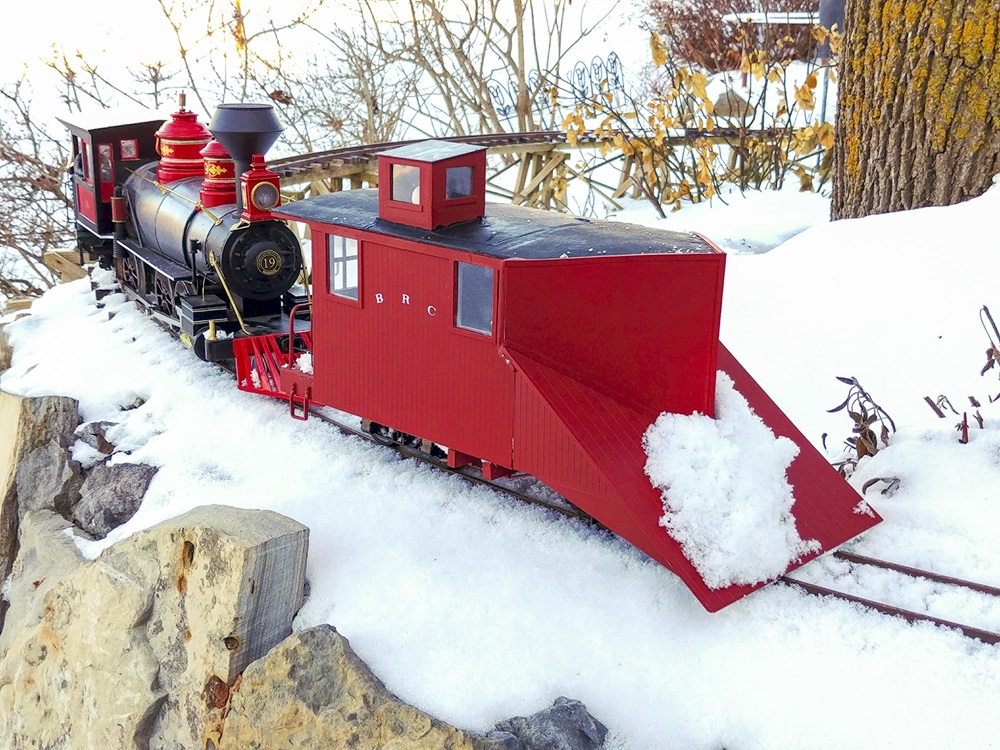 A steam engine pushing a snowplow on a garden layout covered in snow