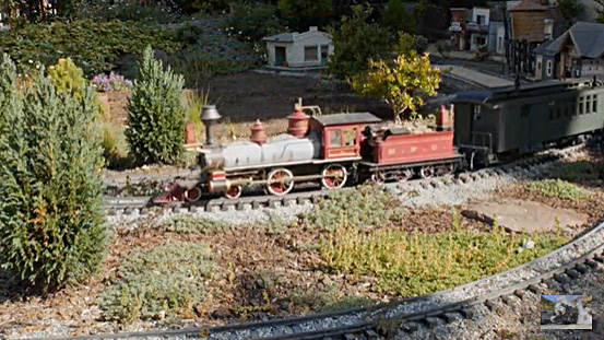 a video screen cap of a steam engine train and some buildings on a garden layout