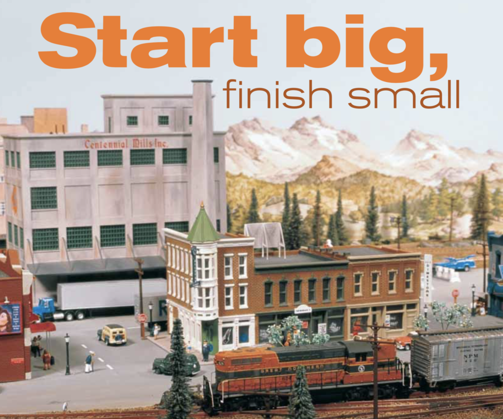 Picture of an N scale small town with a GP7 Great Northern unit in the foreground and an industrial building in the background. The original headline appears in the sky: Start Big, Finish Small.