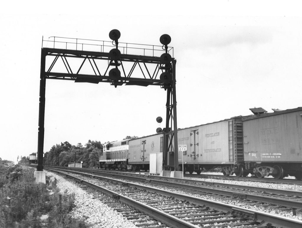 A black and white photo taken from behind a GP7 diesel locomotive as it passes by a stop light