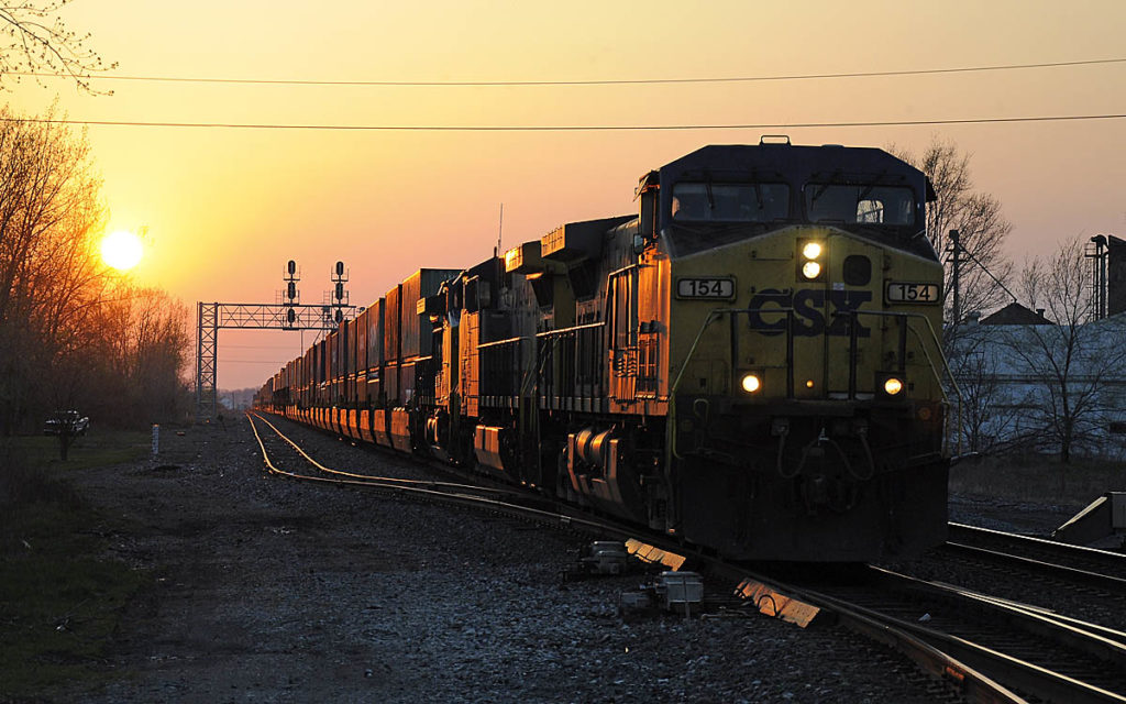 Train under signal bridge coming out of setting sun