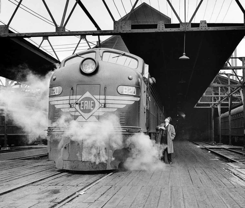 A black and white photo of a conductor posing with a train