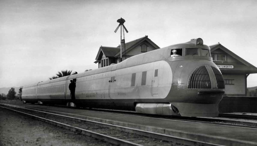 Three-unit streamlined passenger train poses in front of station