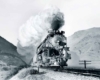 Smoking steam locomotive with passenger train between mountains