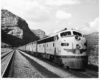 Streamlined diesel locomotives lead passenger train away from mountain cliffs