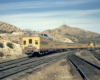Rear of yellow passenger train passing diesel freight locomotive