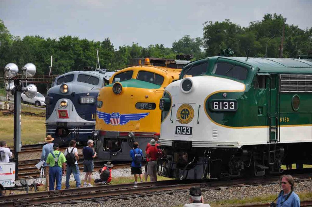 Three streamlined, cab unit locomotives appear before crowds.