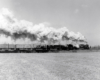 A distant shot of a train passing by with big white smoke coming out of its chimney