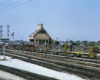 A yellow and black train passing by a coaling tower