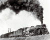A picture of a train passing by a stoplight with big black smoke