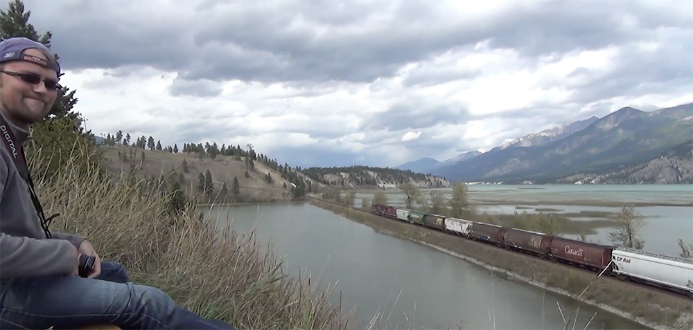 A freight train winds its way beneath cloudy skies on a causeway.