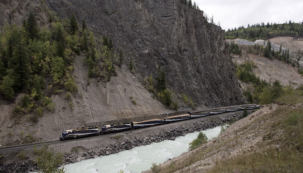 A freight train follows the tracks along a rocky canyon bottom in British Columbia.