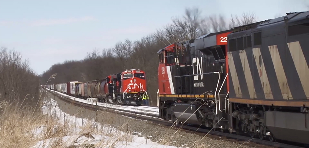 Two red-black-and-white Canadian National locomotives meet in a snow-covered scene.