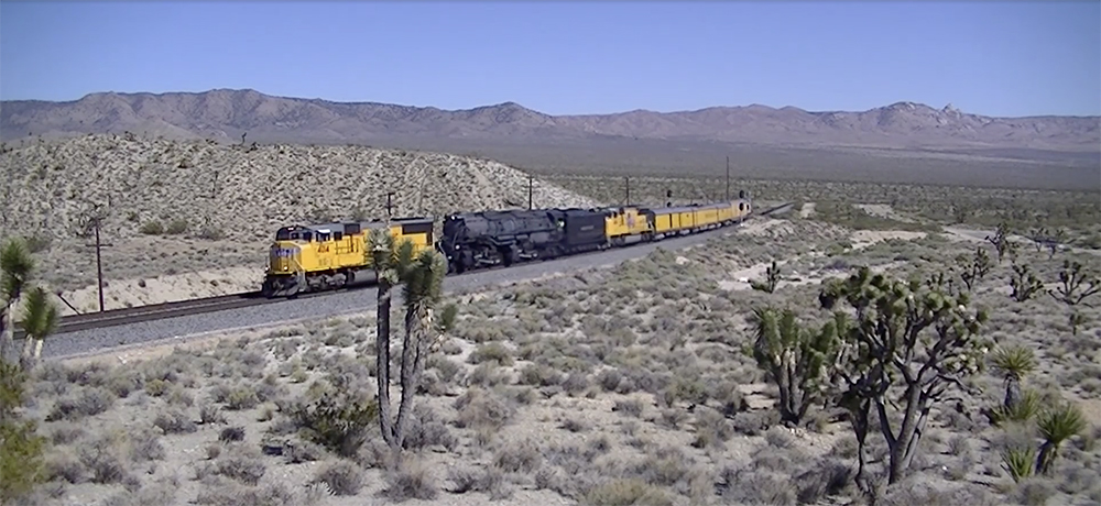 Union Pacific diesel locomotives brace Big Boy No. 4014 in hilly desert terrain.