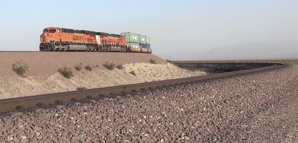 An orange-and-black BNSF Railway freight train winds its way through barren desert.