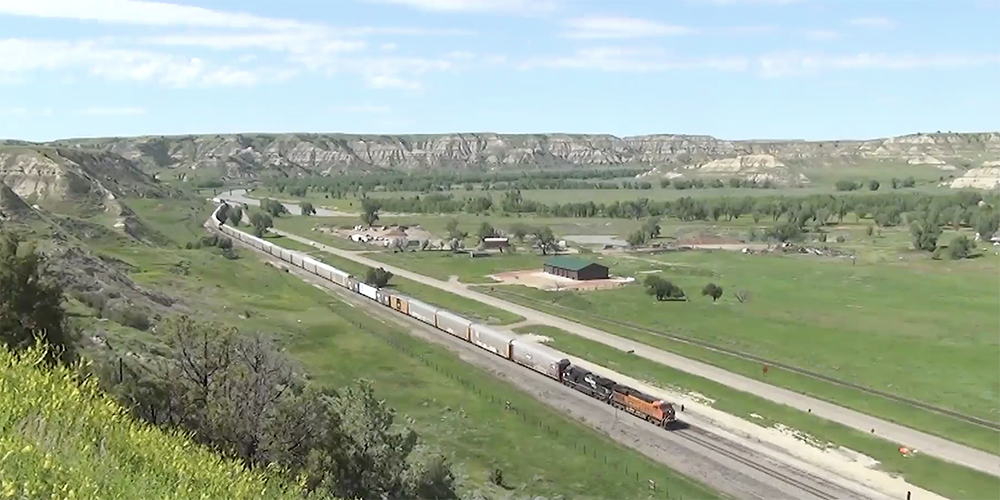 A freight train on a mostly clear day working on a straightaway in green prairie of North Dakota.