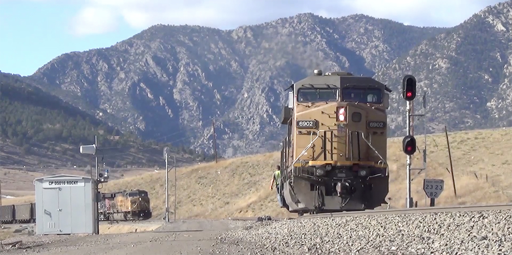 A yellow painted diesel locomotive surrounded by dry land and mountains in the background.