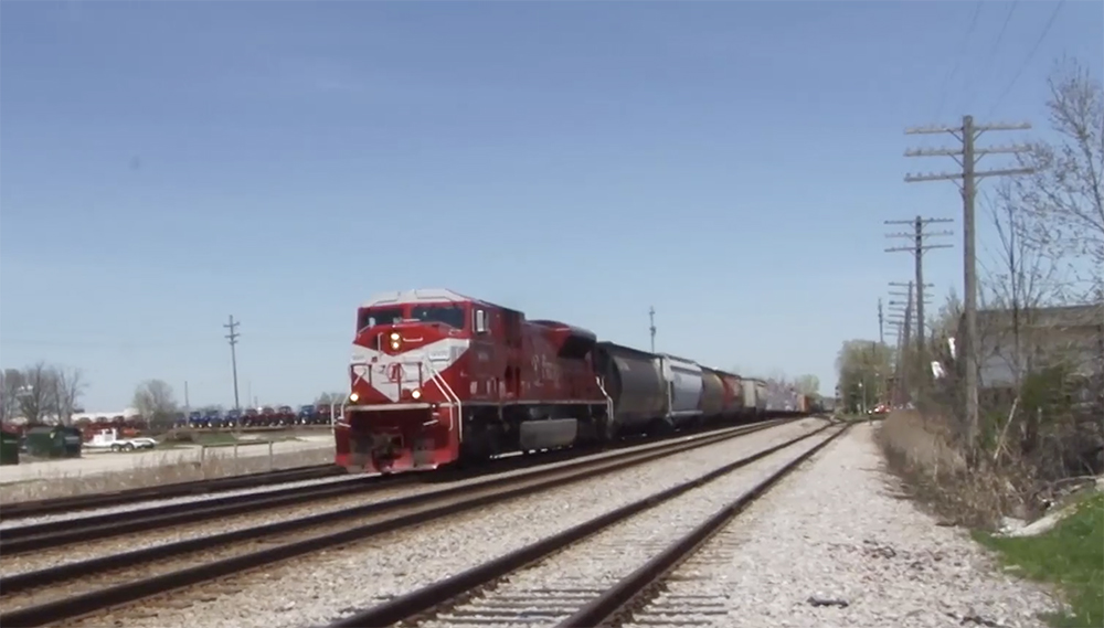 A red-and-gray diesel locomotive leads a freight train across flat territory in Wisconsin.