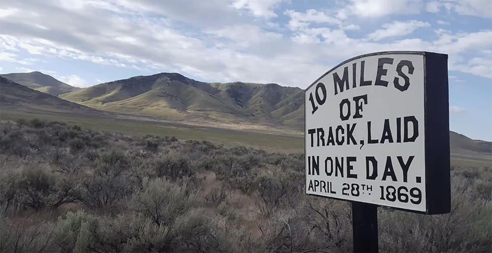 Sign marking where 10 miles of track where laid in one day with desert scrub land and mountains as background.