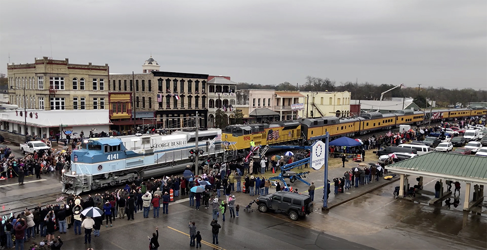 George H.W. Bush commemorative locomotive hauls a yellow passenger train through a Texas town in 2018.