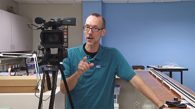 David Popp standing behind a video camera pointing his finger.