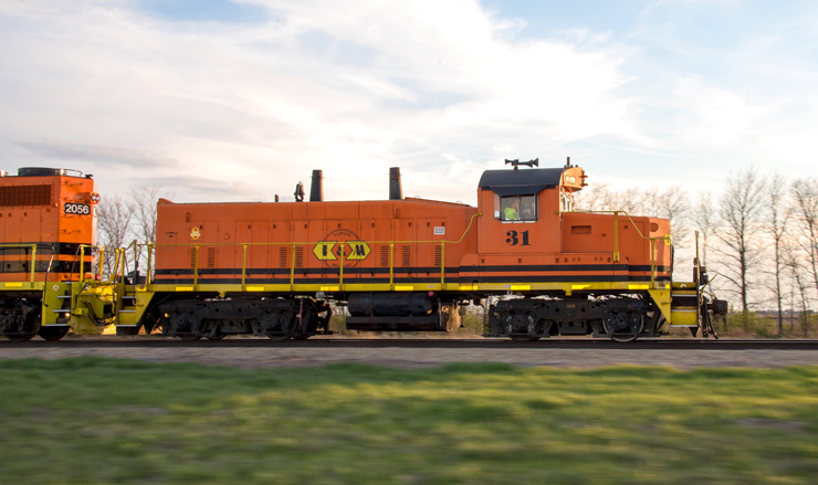 Older orange locomotive leading a train in late afternoon sunlight.