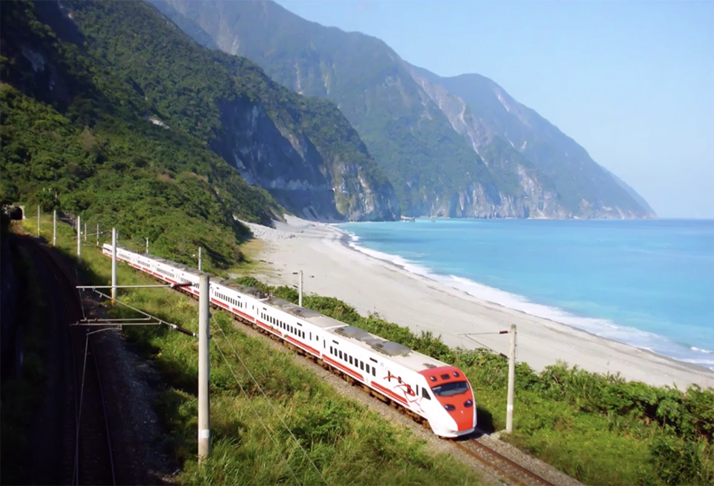 High speed passenger train operating on Taiwan's temperate mountainous coast on a sunny day.