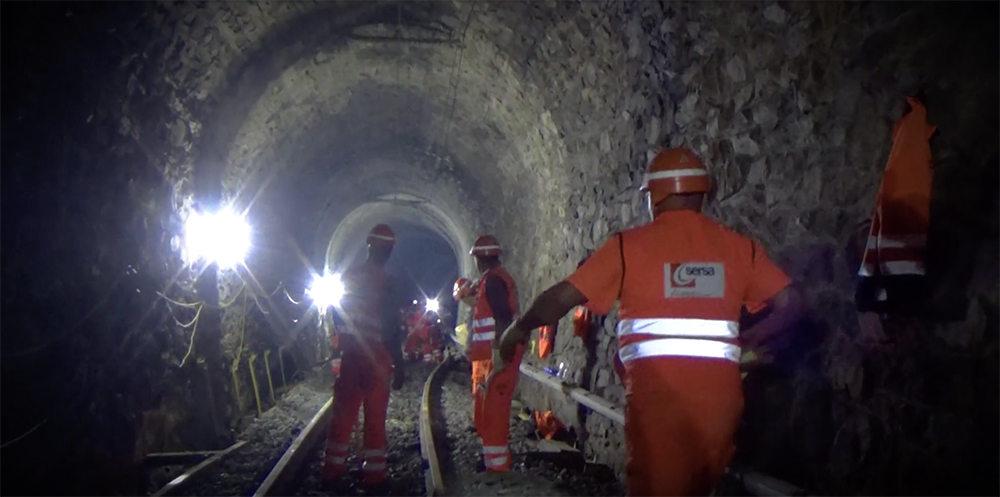 Orange-clad workers in a darkened rail tunnel.