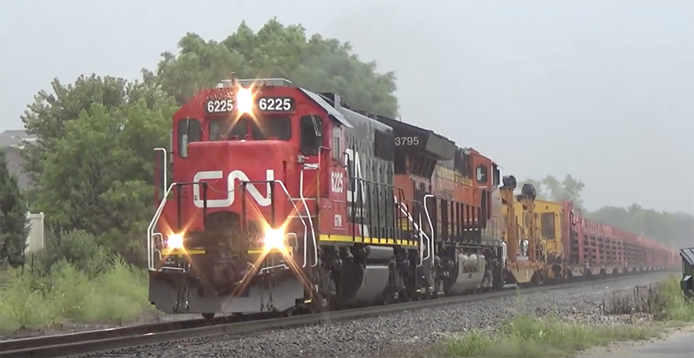 A red-painted Canadian National locomotive hauling a train in the rain.