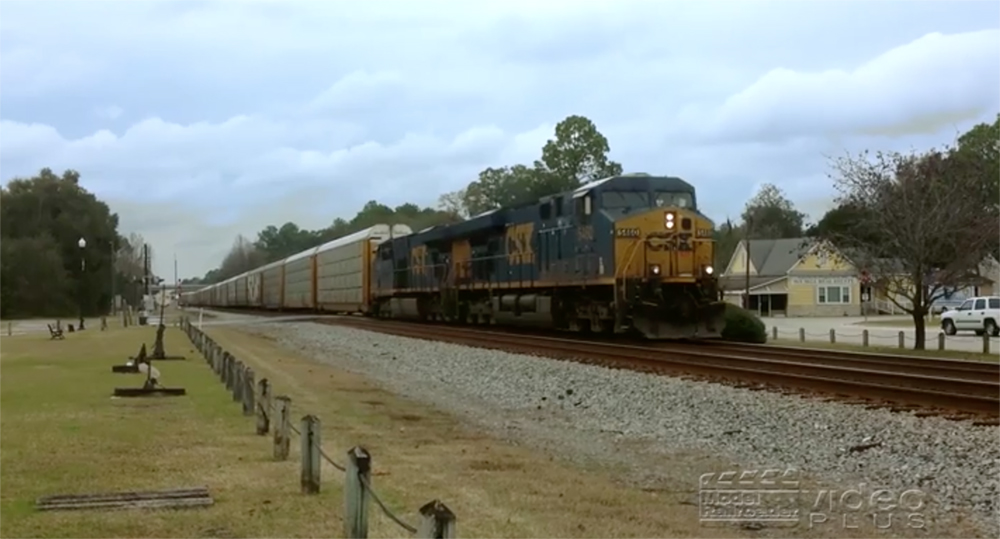 A blue-painted CSX Transportation locomotive moves through a flat landscape with green trees to each side.