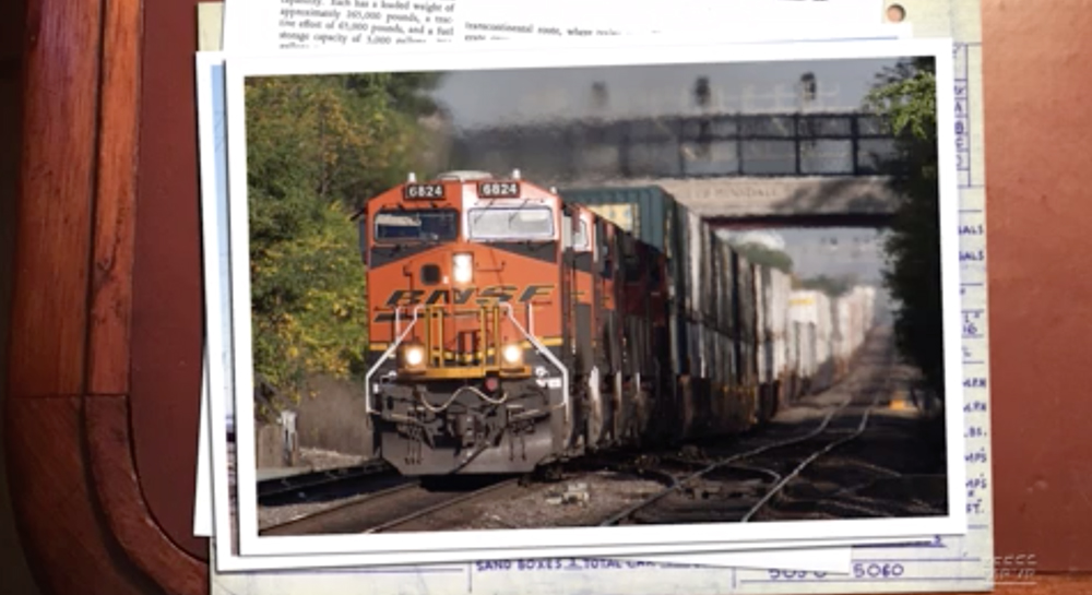 An orange-painted BNSF Railway locomotive leads a freight train with a signal bridge in the background.