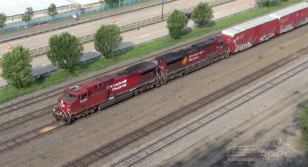 Red-painted Canadian Pacific locomotives haul a train as seen from a high vantage point.