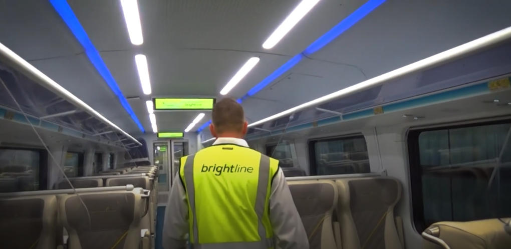 Man in a bright yellow vest walking down the aisle inside of a passenger car