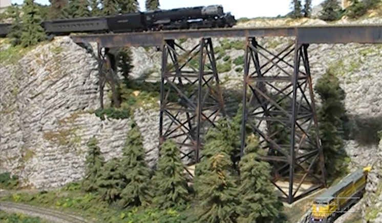 model train pulled by a steam engine crossing a bridge