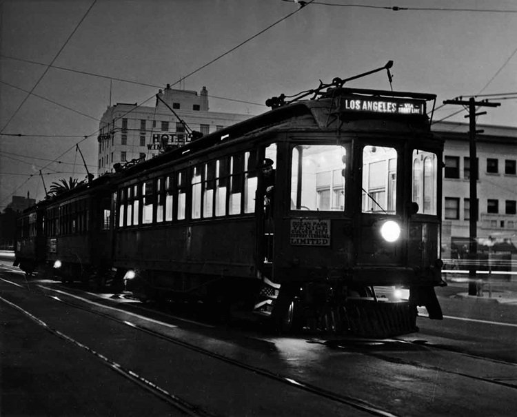 Lighted streetcar train moving over a city street in darkness.