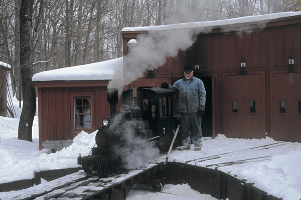 Man in snowy scene with ride on steam locomotive.